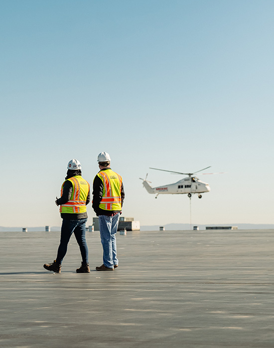 Two Korte employees walking on the roof of a warehouse with a helicopter hovering in the background.