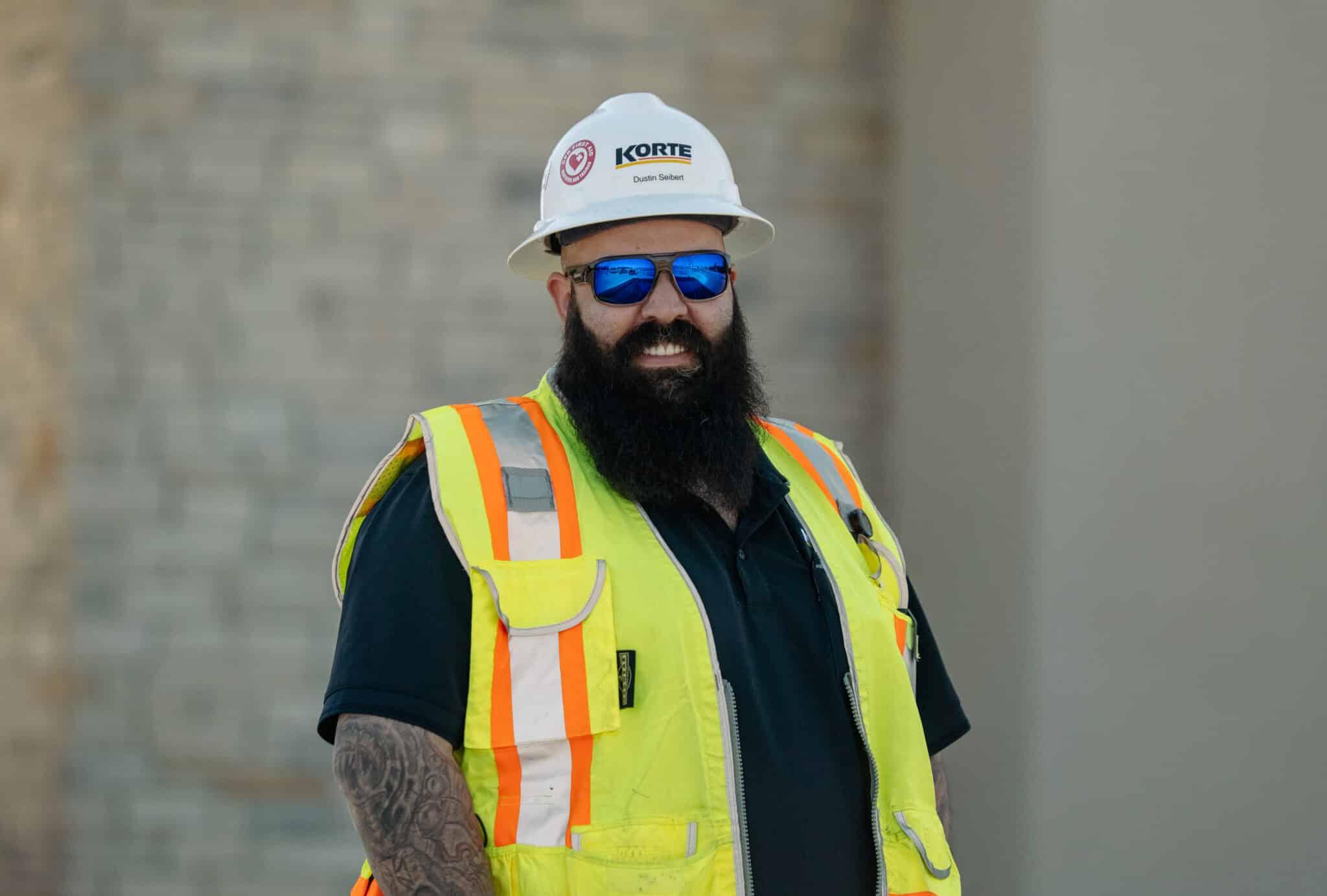 Man with large beard, in hard hat with construction safety vest smiling at camera